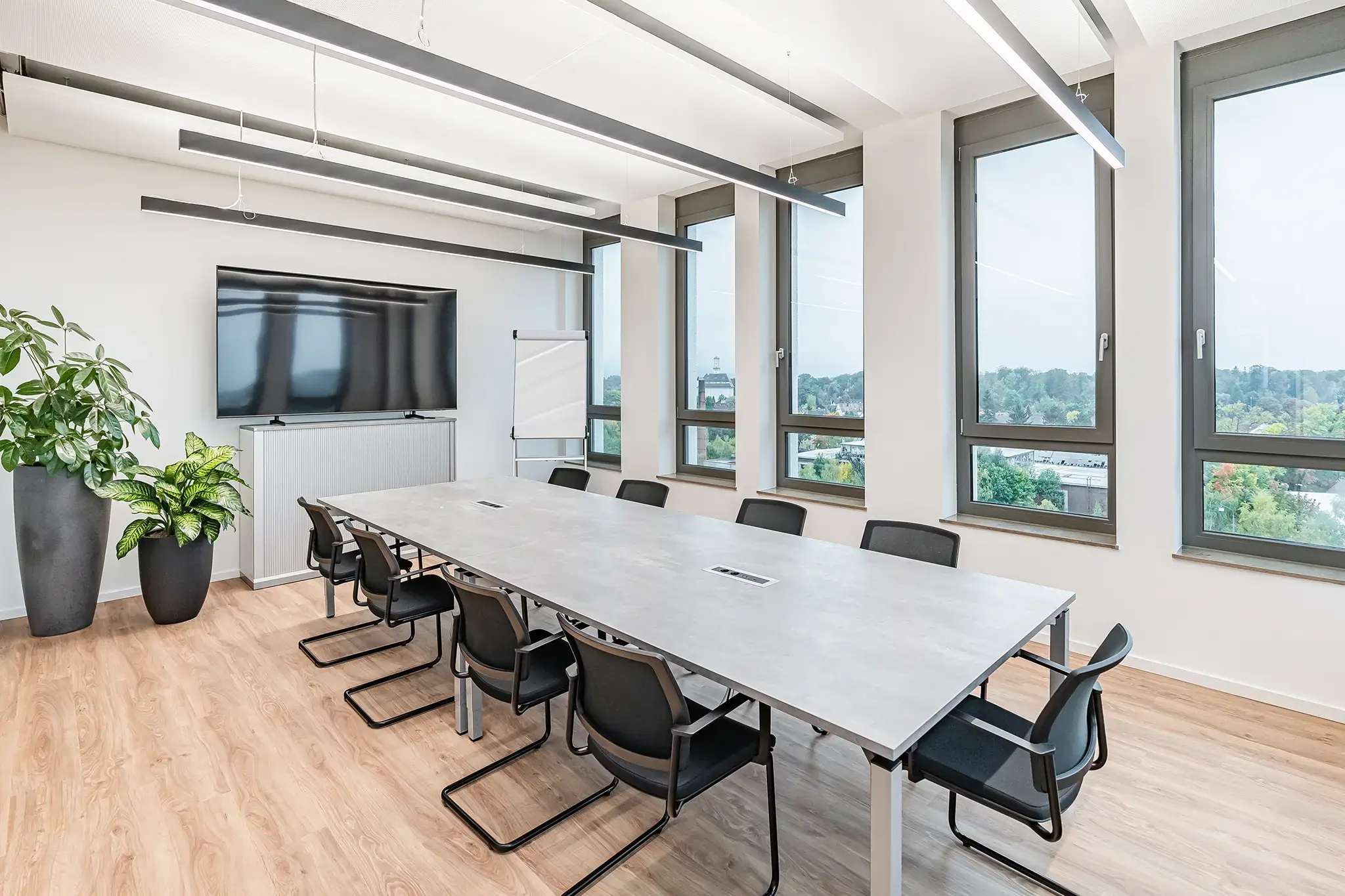 Besprechungsraum im roosi-Büro Rosenheim mit langem Konferenztisch, Bildschirm an der Wand, Flipchart und Fensterfront
